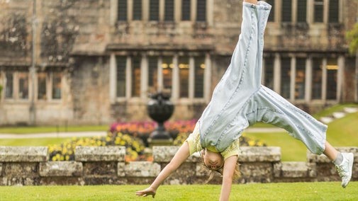 A child cartwheels across the lawn in front of Lanhydrock House on a bright summer day.